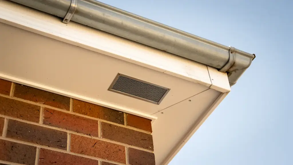 The soffit and gutter corner of a brick house with a fitted mesh vent cover at the eave